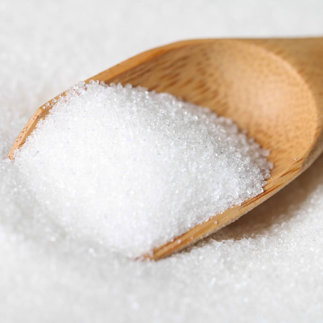 White, sugar-like crystals, displayed on a wooden spoon..