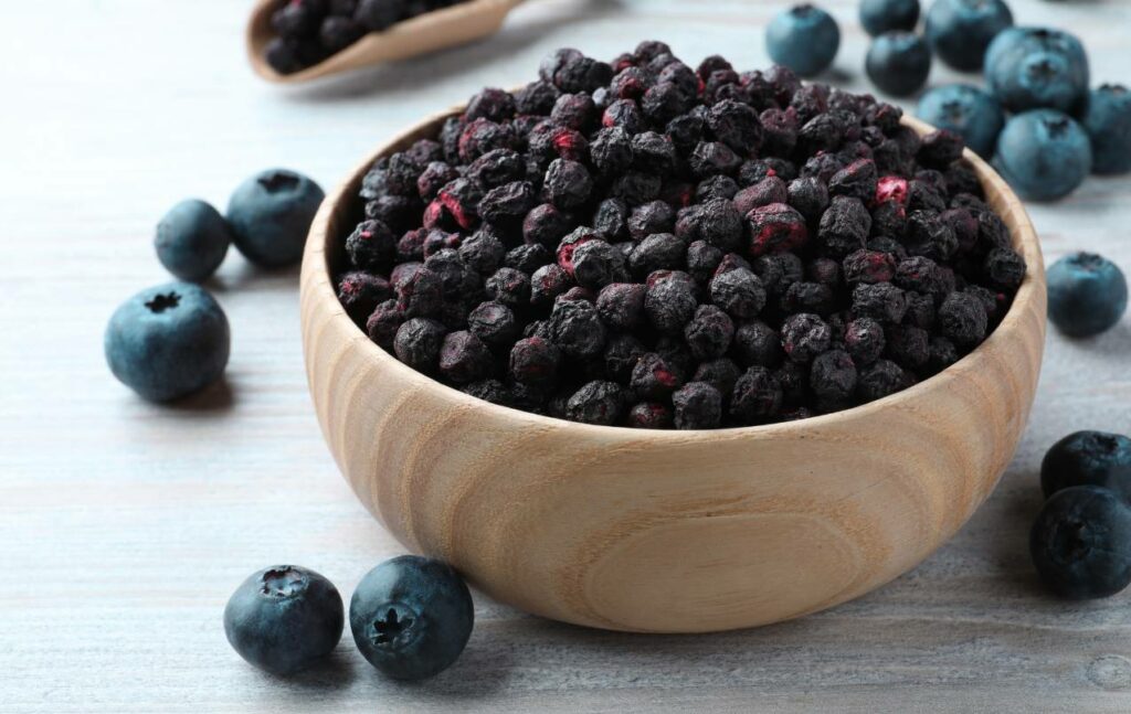 Freeze-dried blackberries in a wooden bowl displayed with fresh blackberry fruit.