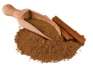 Ground cinnamon displayed with a wooden spoon and cinnamon sticks.