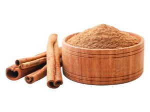 Brown cinnamon powder in a wooden bowl next to three cinnamon sticks.