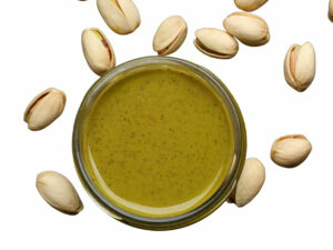 Top view of greenish butter in a bowl surrounded by some pistachio nuts.