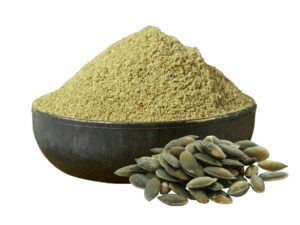 Green powder in a bowl beside some pumpkin seeds.