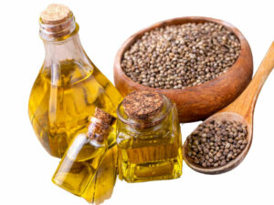 Small brown seeds in a bowl displayed besides bottled oil.