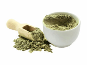 Green powder in a bowl beside a wooden spoon.
