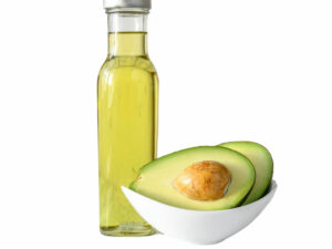 Oil in a transparent bottle beside a bowl with an avocado cut open.