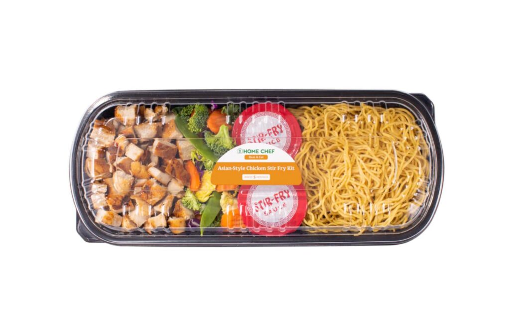 Black plastic container with transparent lid. Chopped chicken, veggies, two sauce packages and noodles.