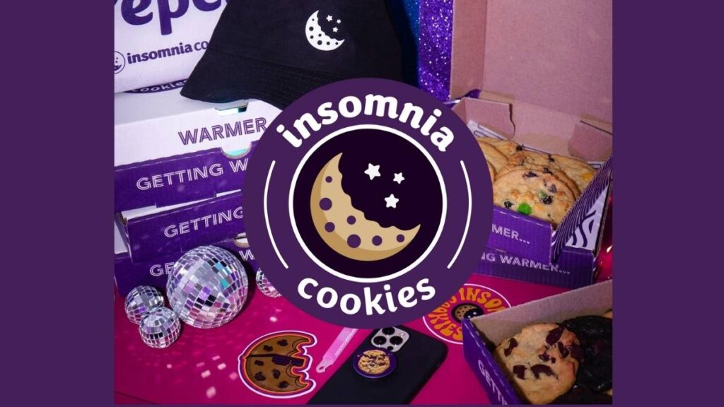 Stack of Insomnia Cookies with branded packaging in the background, highlighting the bakery’s fresh dessert late night offerings.