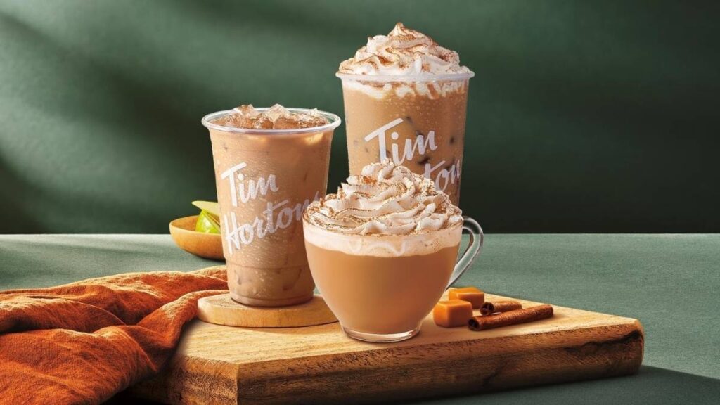 Tim Hortons fall drinks with whipped cream on wooden tray, styled with pumpkin and cozy blanket.