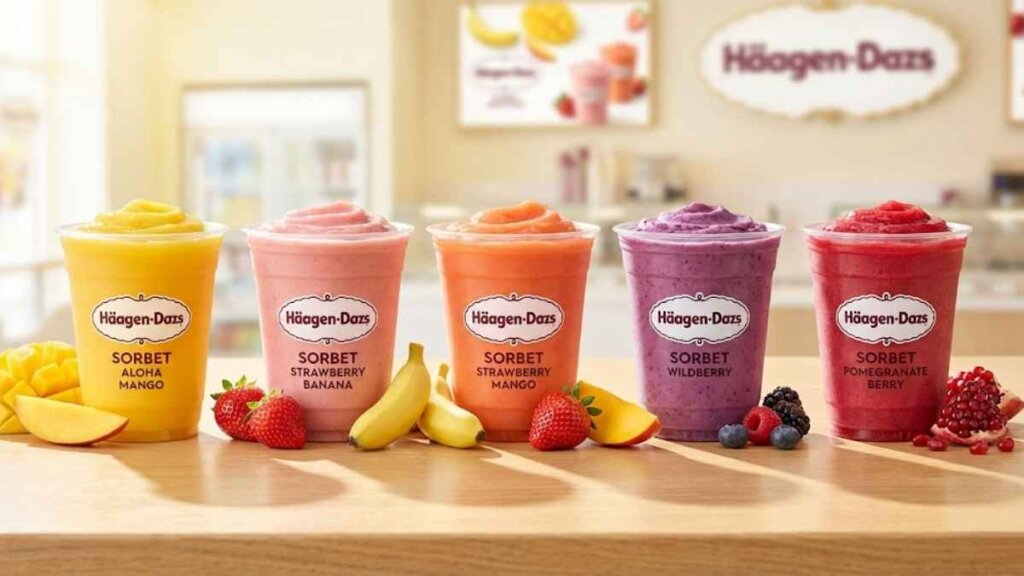 A vibrant marketing image showing a collection of five Häagen-Dazs Sorbet Smoothies arranged against a solid bright blue background. The smoothies range in color from yellow-orange to deep berry red, and fresh ingredients like mango slices, strawberries, and blueberries are scattered artistically around the base of the cups.
