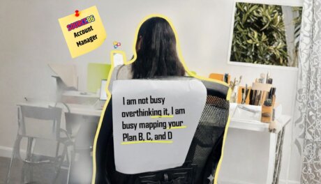 An account manager at the working desk and a sign that says "I am not busy overthinking it, I am busy mapping your Plan B, C and D"