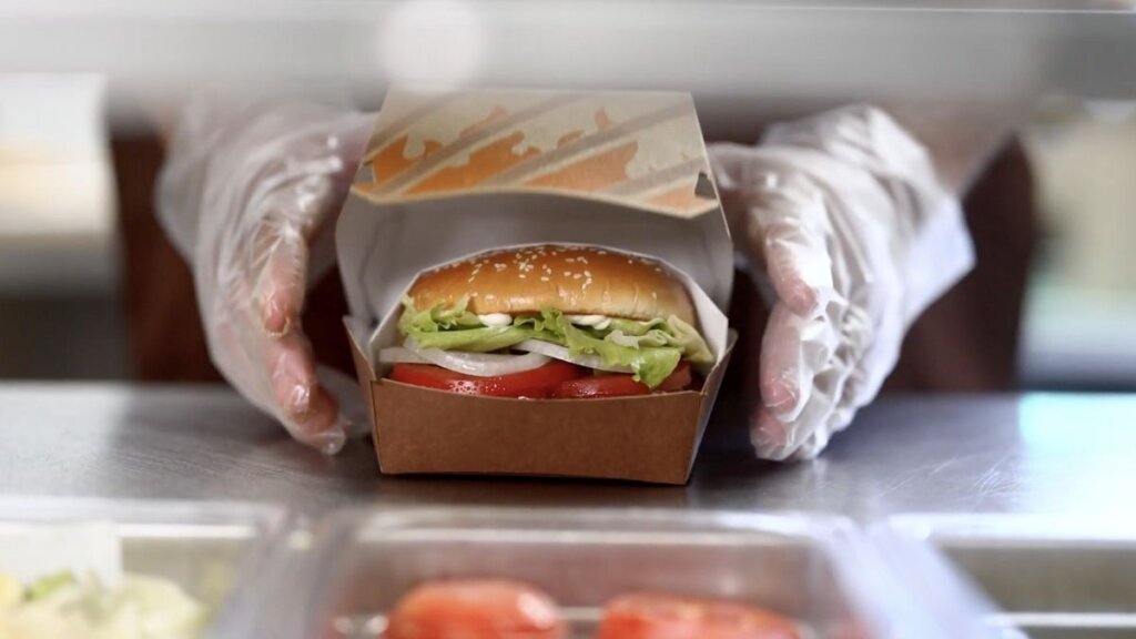 A close-up of the newly elevated Burger King Whopper, featuring a premium bun, flame-grilled beef patty, fresh lettuce, tomatoes, and onions, sitting inside its new protective box packaging.