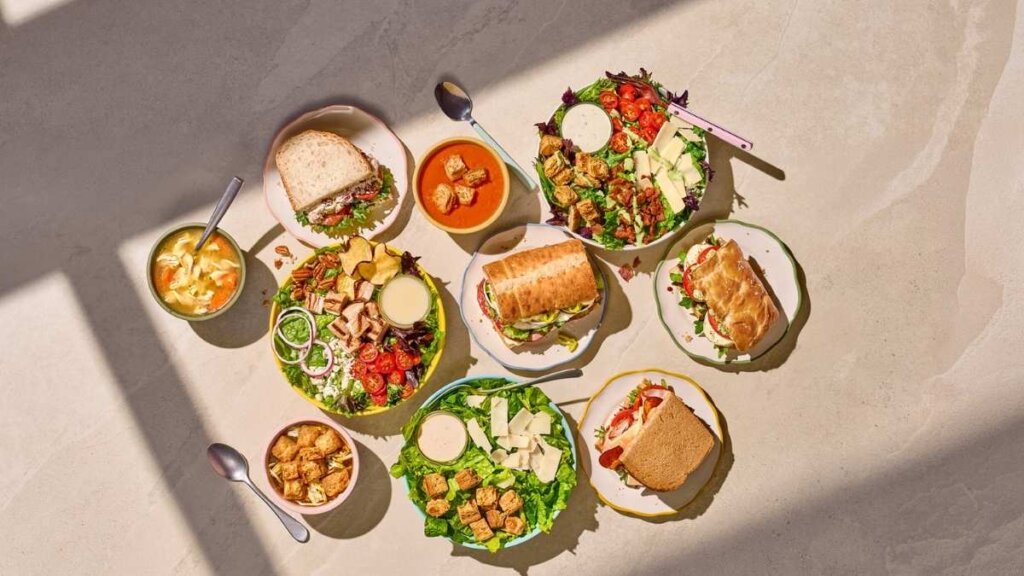 A spread of Panera Bread Mix & Match menu items, including a cup of Creamy Tomato Soup, a half Bacon Turkey Bravo sandwich, and a half Fuji Apple Chicken Salad, arranged on a wooden table with a price tag graphic reading "$4.99 Each."