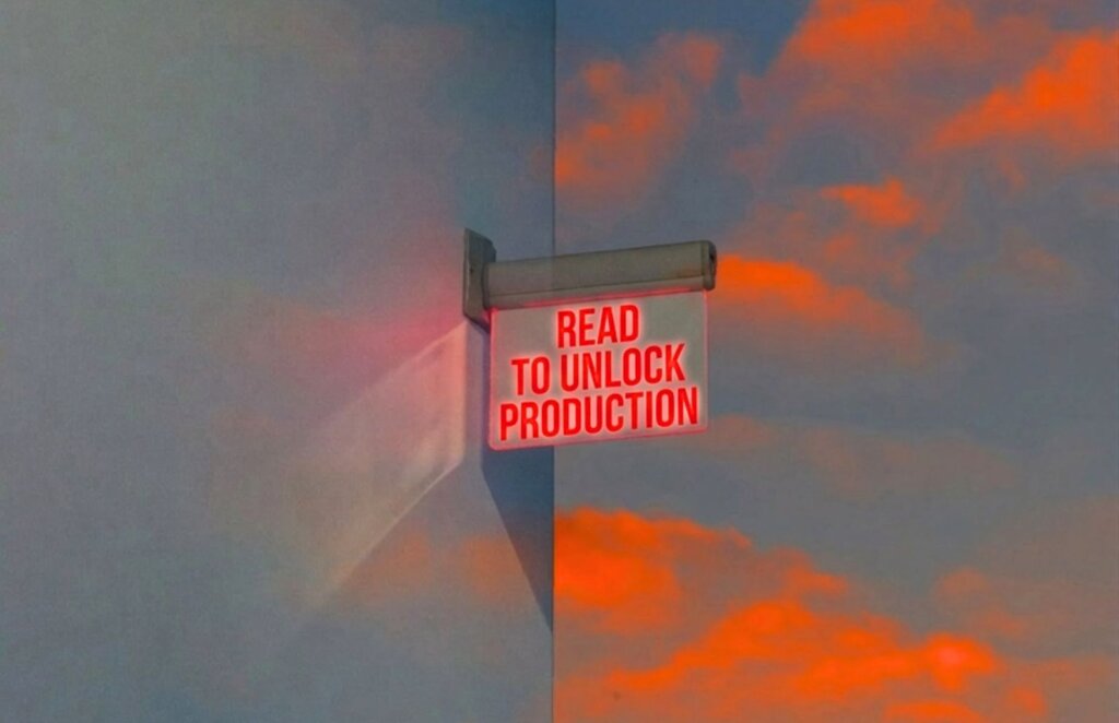 A sign with red neon letters reading "READ TO UNLOCK PRODUCTION" is mounted on a corner wall, set against a backdrop of a surreal sky with glowing orange clouds and a soft blue haze.