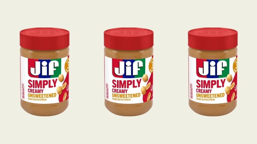 A jar of Jif Simply Unsweetened Creamy peanut butter next to a bowl of fresh roasted peanuts.